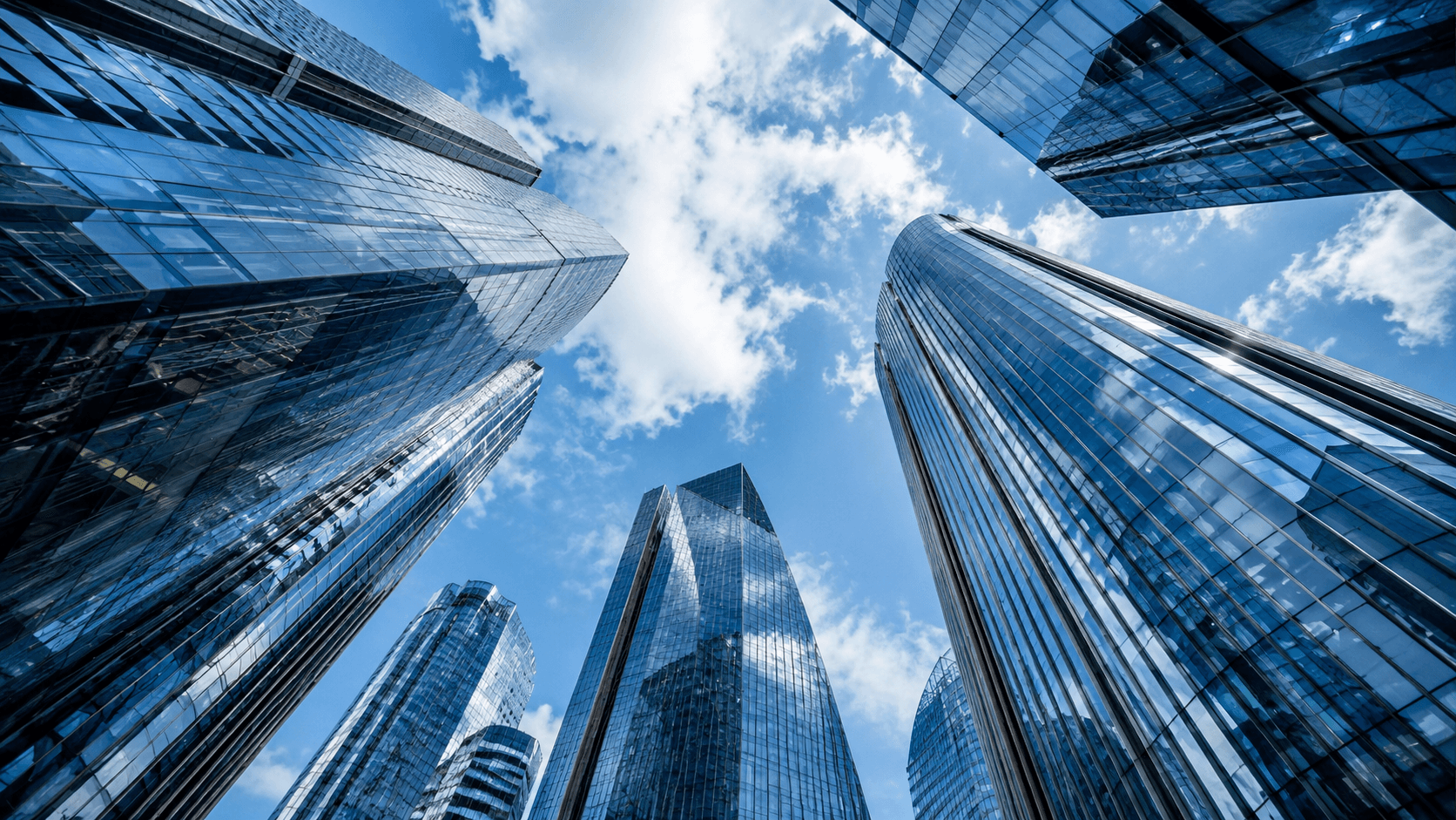 Blue glass towers viewed from below against a bright sky